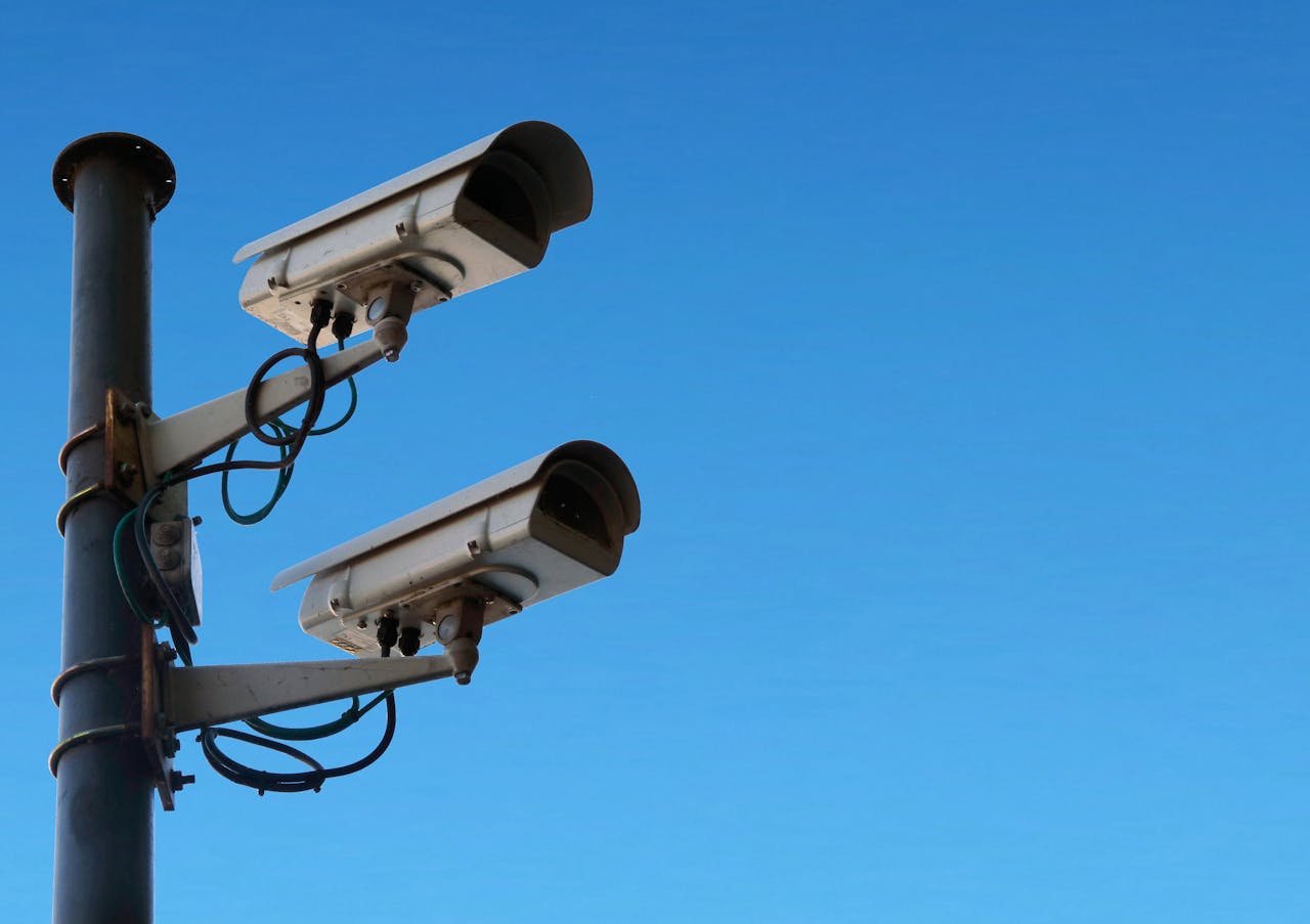 Two security cameras mounted on a pole with a bright blue sky as the backdrop.
